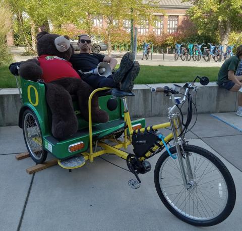 Bike Program Manager sitting next to a large stuffed teddy bear in a UO branded pedicab